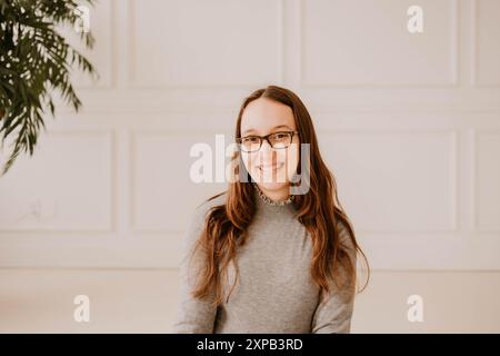 Lächelnde junge hispanische Frau in grauem Pullover, saubere Inneneinrichtung Stockfoto