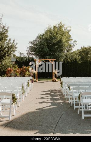 Hochzeitszeremonie im Freien mit weißen Stühlen und Blumenbogen Stockfoto