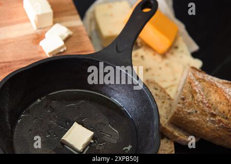 Pfanne mit Butter, Brot und Käse auf einem Holzbrett Stockfoto