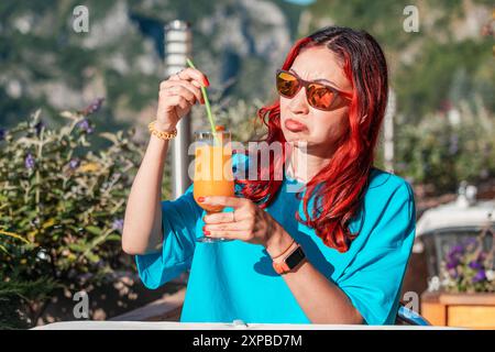 Eine Frau mit einem ekelhaften Ausdruck, die auf einen verdorbenen Orangensaft reagiert und den unangenehmen Geschmack und Geruch des Getränks hervorhebt. Stockfoto