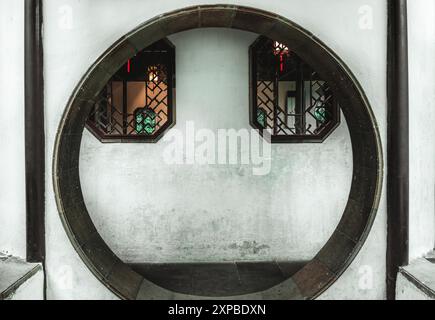Ein kreisförmiger Eingang in einer weißen Wand, mit zwei achteckigen Fenstern, eingerahmt in dunklem Holz, auf beiden Seiten der Öffnung. Stockfoto