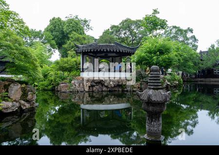 Suzhou, China - 11. Juni 2024 : Ein chinesischer Gartenpavillon überblickt einen Teich, der von üppigem Grün umgeben ist. Stockfoto