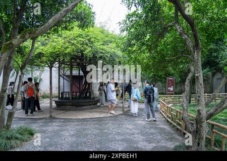 Suzhou, China - 11. Juni 2024 : Eine Gruppe von Menschen spaziert durch einen traditionellen chinesischen Garten in Suzhou, China, der von üppigen Bäumen beschattet wird. Stockfoto