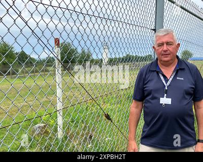Rasdort, Deutschland. August 2024. Der ehemalige Bundesgrenzschutz Stefan Czeloth steht am Zaun des ehemaligen US-Lagers Point Alpha, das heute eine Gedenkstätte ist. Die ehemalige innerdeutsche Grenze verlief direkt hinter dem Zaun am weißen und roten Pfosten. Czeloth patrouillierte dort oft. Eine neue Sonderausstellung im Point Alpha erinnert an die Geschichte des Bundesgrenzschutzes. Im Hintergrund ist ein ehemaliger DDR-Wachturm zu sehen. Quelle: Michael Bauer/dpa/Alamy Live News Stockfoto