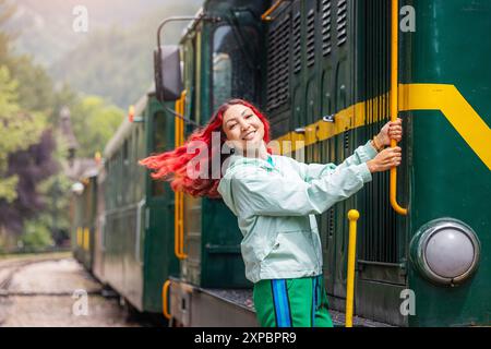 Passagiermädchen in lässiger Kleidung, Ankunft am historischen Bahnhof Mokra Gora, begrüßt vom Charme des alten Lokomotivzuges und des alten Wagens. Stockfoto