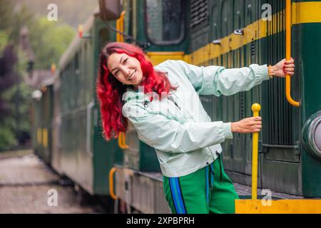 Passagiermädchen in lässiger Kleidung, Ankunft am historischen Bahnhof Mokra Gora, begrüßt vom Charme des alten Lokomotivzuges und des alten Wagens. Stockfoto