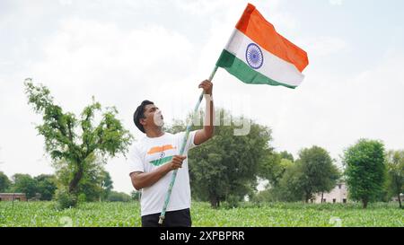 Kinder mit Familienmitgliedern tragen T-Shirt mit indischer Flagge und halten, winken oder laufen mit Tricolor mit Grün im Hintergrund, feiern Stockfoto
