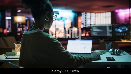 Rückblick: Motivierte schwarze Frau, die am Abend in Kreativagentur Laptop benutzt, Manager arbeitet an der Umsetzung der Geschäftsstrategie für Kunden. Spezialist Für Projektpläne Stockfoto