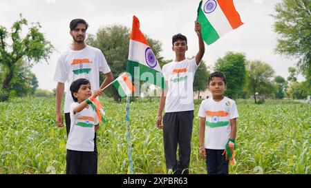 Kinder mit Familienmitgliedern tragen T-Shirt mit indischer Flagge und halten, winken oder laufen mit Tricolor mit Grün im Hintergrund, feiern Stockfoto