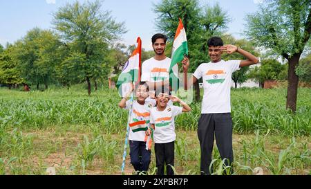 Kinder mit Familienmitgliedern tragen T-Shirt mit indischer Flagge und halten, winken oder laufen mit Tricolor mit Grün im Hintergrund, feiern Stockfoto