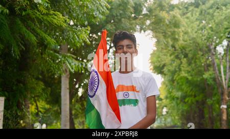 Kinder mit Familienmitgliedern tragen T-Shirt mit indischer Flagge und halten, winken oder laufen mit Tricolor mit Grün im Hintergrund, feiern Stockfoto