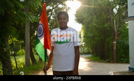 Kinder mit Familienmitgliedern tragen T-Shirt mit indischer Flagge und halten, winken oder laufen mit Tricolor mit Grün im Hintergrund, feiern Stockfoto