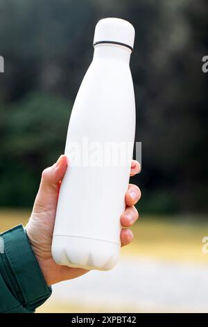 Der Mann hält eine Modell-Thermoskanne gegen verschwommene Büsche aus der Nähe Stockfoto