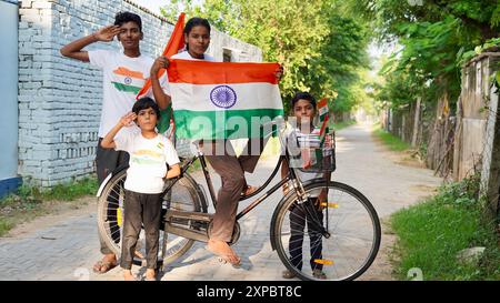 Kinder mit Familienmitgliedern tragen T-Shirt mit indischer Flagge und halten, winken oder laufen mit Tricolor mit Grün im Hintergrund, feiern Stockfoto