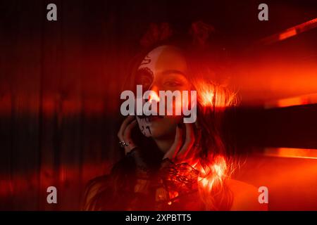 Frau mit kompliziertem Sugar Skull Make-up, beleuchtet von dramatischer roter Beleuchtung, die eine eindringliche und künstlerische Atmosphäre einfängt. Stockfoto