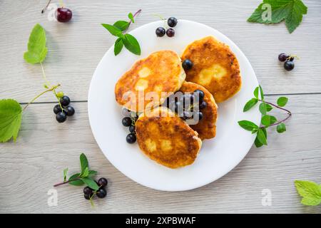 Frittierte Quark-Pfannkuchen mit schwarzen Johannisbeeren auf einem Holztisch. Stockfoto