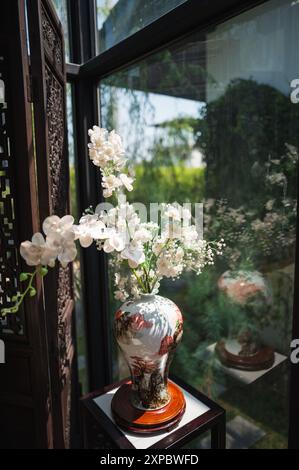 Die Vase im alten chinesischen Stil mit künstlich blühenden weißen Blumen in der Glasecke. Stockfoto
