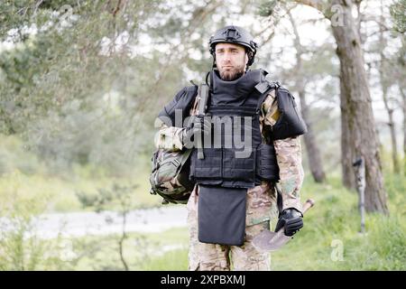 Ein junger Soldat in Uniformen und taktischer Weste arbeitet im Wald und bereitet sich auf die Aktion an einem temporären Waldstützpunkt vor. Ein Mann tut es bei der Minenräumung Stockfoto