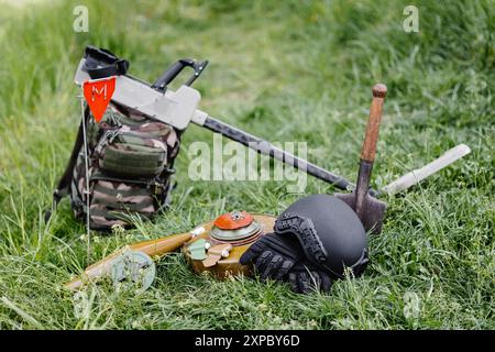 Sprengkörper und ein Metalldetektor liegen auf dem Hintergrund eines Waldmassivs. Ausrüstung für die Minenräumung des Gebiets. Stockfoto