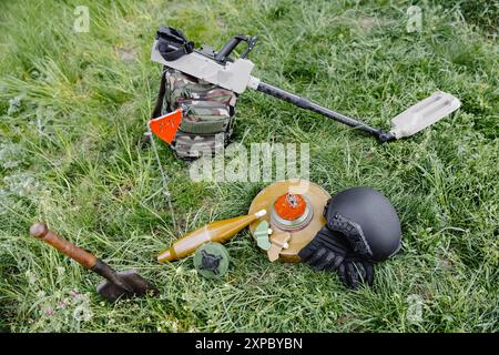 Sprengkörper und ein Metalldetektor liegen auf dem Hintergrund eines Waldmassivs. Ausrüstung für die Minenräumung des Gebiets. Stockfoto