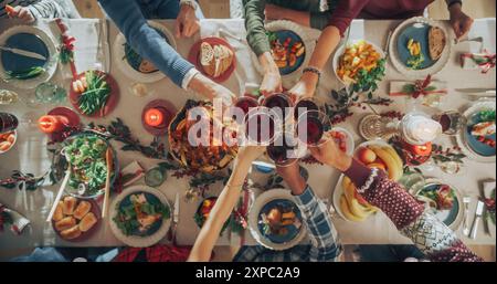 Eltern, Kinder und Freunde genießen gemeinsam das Weihnachtsessen in einem gemütlichen Zuhause. Verwandte, die Mahlzeiten teilen, Gläser mit Rotwein aufziehen, Toasten, Feiertage feiern. Top-Down-Ansicht Stockfoto