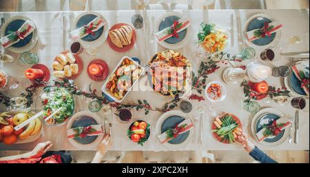 Restaurant bereitet ein Weihnachtsessen vor. Anonyme Leute servieren Essen, Putenbraten und andere Gerichte auf dem Esstisch mit dekorativen Preiselbeerbüschen und Kerzen. Top-Down-Aufnahme Stockfoto