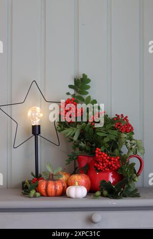 Herbststillleben mit rowan, dekorativen Keramikkürbissen und Kerze auf hellgrünem hölzernem Hintergrund. Dekorationen im Herbst. Stockfoto