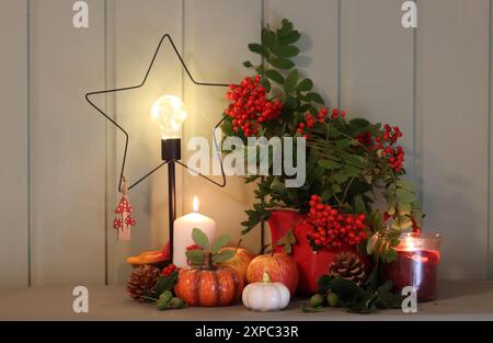 Weihnachtsdekoration auf einer Kommode mit Kerzen, vogelbeeren und einer sternförmigen LED-Laterne. Grüner Holzhintergrund mit Kopierraum. Stockfoto