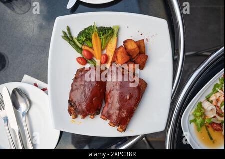 Gegrillte Schweinerippchen mit spezieller marinierter grillsoße, Pommes Frites und Gemüse auf weißem Teller im Restaurant Stockfoto