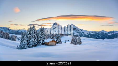 Panoramablick auf die Seiser Alm mit kleinem Holzblockhaus und ersten Schnee. Schneebedeckte Hügel mit orangener Lärche und Langkofel-Berggruppe. Seiser Alm, Dolomiten, Italien. Stockfoto