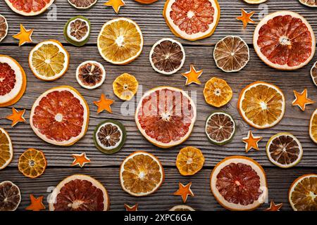 Getrocknete Orangen-, Grapefruit-, Zitronen- und Limettenscheiben mit Orangenschalen-Sternen auf rustikalem Holzbrett. Weihnachten oder Neujahr Ornament Border Hintergrund Stockfoto