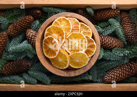 Getrocknete Orangenscheiben in Holzkiste mit Tannenzweigen und Tannenzapfen aus nächster Nähe. Weihnachten oder Neujahr Hintergrund Stockfoto