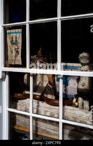 Kuriositäten und Antiquitäten sitzen hinter dem Fenster eines Architektenbüros in Southwold, England. Farbenfroh, Retro, künstlerisch, stilvoll, antik. Stockfoto