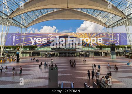 MÜNCHEN, DEUTSCHLAND - 3. AUGUST 2024: Außenansicht des Münchner Flughafens mit Passagieren im Hintergrund. Anschluss suqare zwischen Klemme 1 und 2 mit l Stockfoto