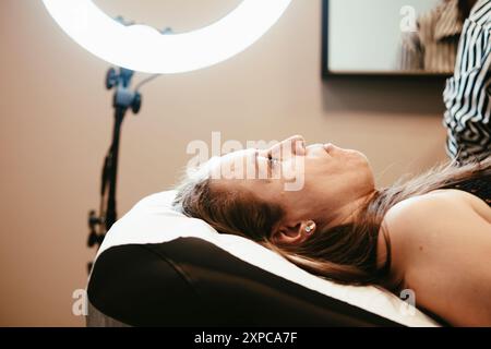 Die Kundin fühlt sich entspannt und verwöhnt, während eine Kosmetikerin in einem gemütlichen Salon Permanent Make-up auf ihre Augenbrauen aufträgt. Die Prozedur verstärkt ihre natürliche Schönheit Stockfoto