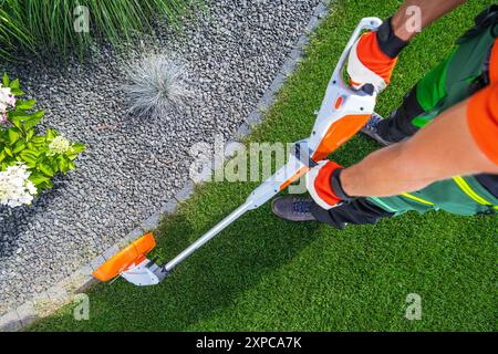 Eine Person schneidet in einem gepflegten Garten mit einem Fadenschneider Rasenkanten auf einem Weg. Stockfoto