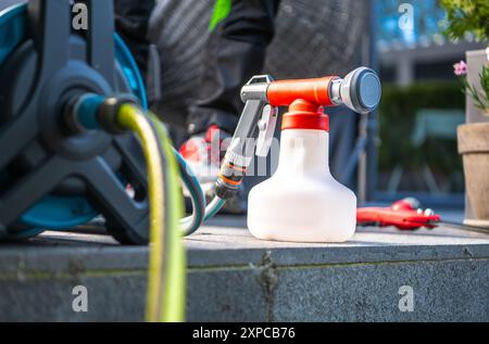 Eine Gartenspritze steht auf einer Steinoberfläche neben einem Gartenschlauch und einer Bewässerungsausrüstung und ist einsatzbereit. Stockfoto