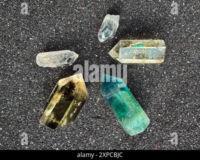 Verschiedene natürliche Edelsteine auf schwarzem Sand Hintergrund: Vielfalt der Kristalle in verschiedenen Formen und Farben Stockfoto