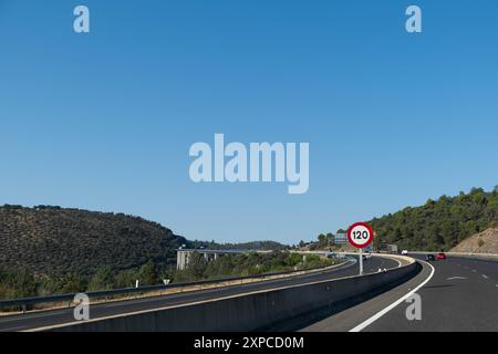 Panoramablick auf eine riesige gekrümmte Autobahn mit einer großen Brücke im Hintergrund in Spanien. Der Tag ist klar und sonnig und der Himmel ist blau. Es gibt eine spe Stockfoto