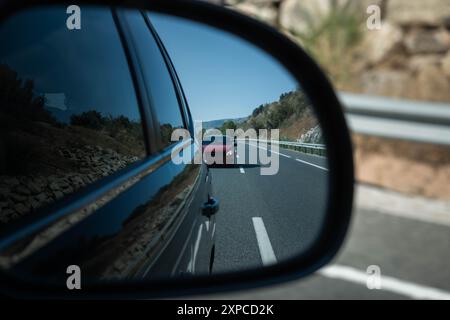 Ein rotes Auto nähert sich von hinten durch den rechten Rückspiegel eines Autos. Vorsicht, Fahrverhalten, Sicherheit und Aufmerksamkeit auf der Straße Stockfoto