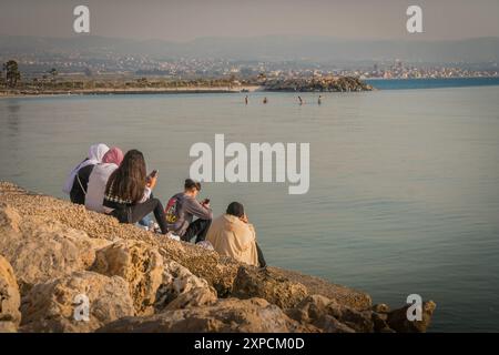 Junge Araber am felsigen Ufer des Mittelmeers im Libanon mit dem Panorama der Stadt Tyrus (Sour). Stockfoto