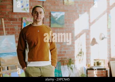 Mittleres Porträt eines jungen kaukasischen Mannes in lässigen Kleidern, stehend mit Händen in Taschen in seinem Kunststudio, Kopierraum Stockfoto