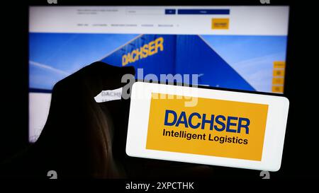 Person mit Smartphone mit Logo des deutschen Logistikunternehmens Dachser Group SE Co. KG vor der Website. Schwerpunkt auf dem Display des Telefons. Stockfoto