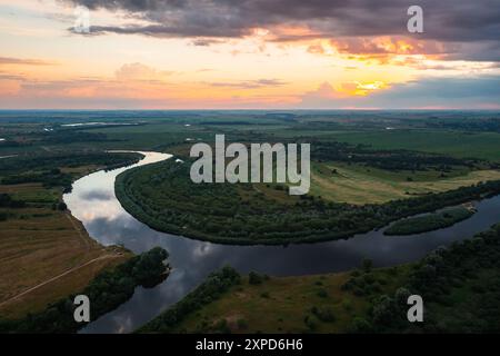 Ein Blick aus der Luft zeigt einen atemberaubenden Sonnenuntergang über einem Fluss, der sich anmutig durch eine üppige Landschaft schlängelt Stockfoto