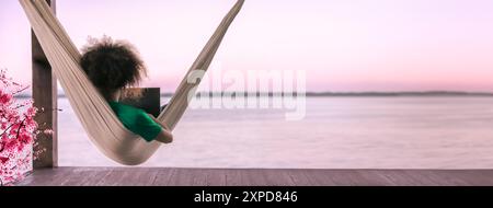 Junger, digitaler Nomade freiberuflicher Mann, der auf einem Laptop unterwegs ist und arbeitet, der in einer Hängematte am Meer an einem tropischen Strand liegt. Fernarbeitskonzept Stockfoto