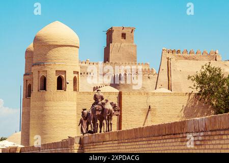 Skulpturengruppe einer Karawane mit Kamelen, die Güter entlang der Seidenstraße in der Nähe der alten Stadtmauern transportieren. Chiwa, Usbekistan - 17. Juli 2024. Stockfoto