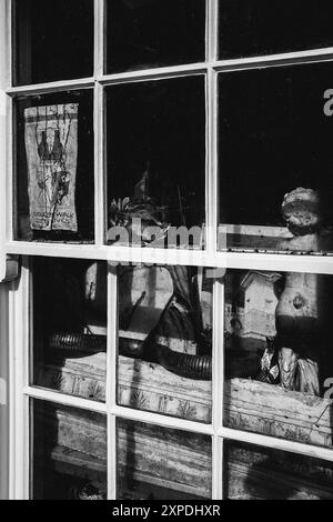 Kuriositäten und Antiquitäten sitzen hinter dem Fenster eines Architektenbüros in Southwold, England. Monochrom, Retro, künstlerisch, Stil, antik. Stockfoto