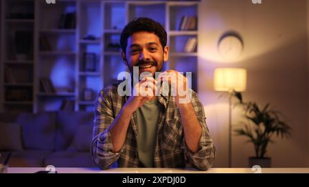 Der junge Araber hat einen Videoanruf mit Freunden, Familie, während er abends am Tisch im Wohnzimmer sitzt. Glücklicher Mann, der in die Kamera lächelt Stockfoto