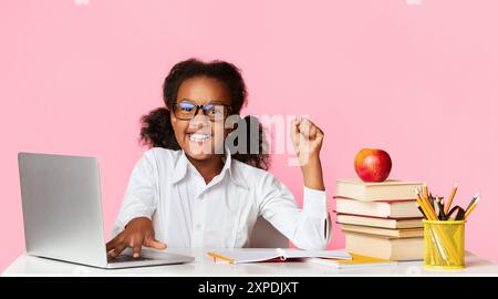 African American School Girl Bei Laptop Raising Hand, Gelber Hintergrund Stockfoto