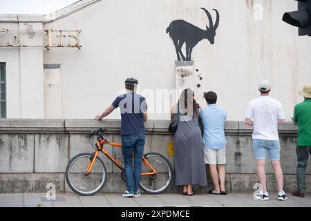 London, Großbritannien. August 2024. Die Leute fotografieren das neueste Kunstwerk des Street Artist Banksy, das eine Bergziege zeigt, die auf der Säule eines Gebäudes thront und Felsen an der Kew Bridge herunterfallen. Quelle: Justin Ng/Alamy Live News. Stockfoto